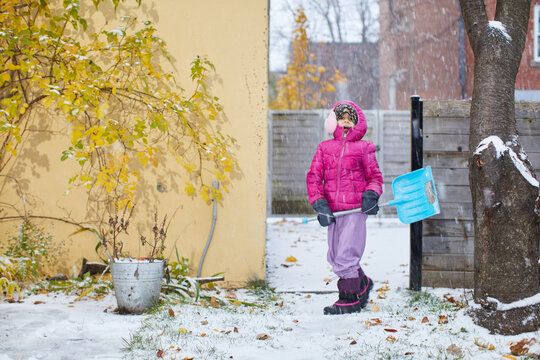 Child in pink puffer jacket and purple snow pants shovels snow