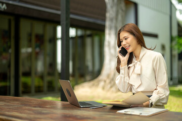 Asian businesswoman talking on phone working remotely outdoors