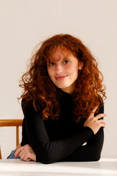 Girl With Curly Hair Poses at a Table in a Brightly Lit Room