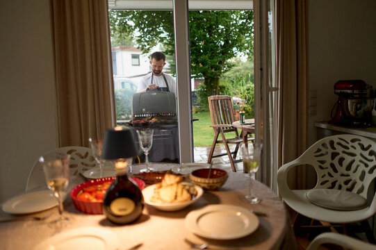 Cozy Dinner Table Set While Man Prepares BBQ Outdoors