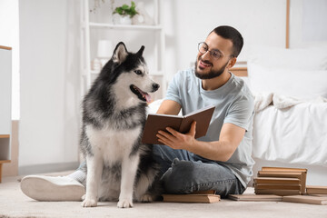 Handsome young man and cute husky dog reading books on floor in bedroom © Pixel-Shot