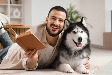 Handsome young man lying on floor and reading book with cute husky dog at home © Pixel-Shot