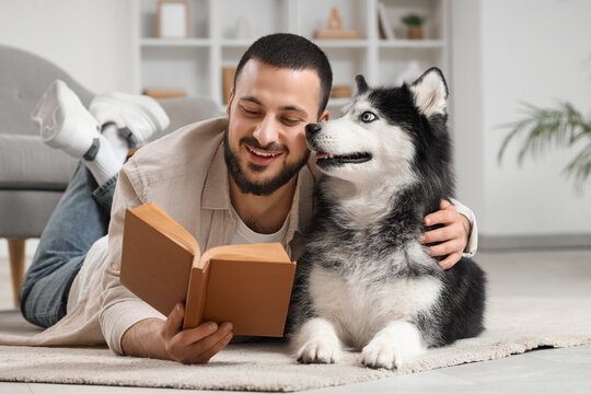 Handsome young man lying on floor and reading book with cute husky dog at home