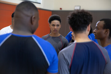 African American teenage males huddling in gymnasium, teen wearing grey athletic top with red seams