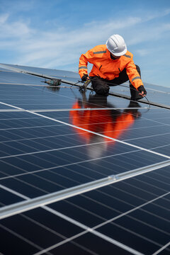 Technician installing solar panels on factory roof for green energy. A skilled technician in safety gear is working on a solar panel installation on rooftop.