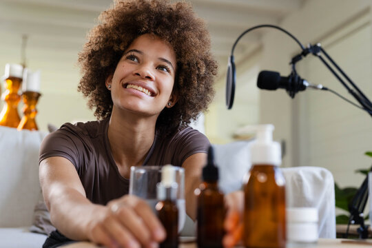 African American woman smiling and demonstrating skincare products on sofa with mic on boom arm