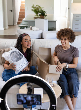 African American women unboxing bubble-wrapped appliance on sofa filming with ring light and phone