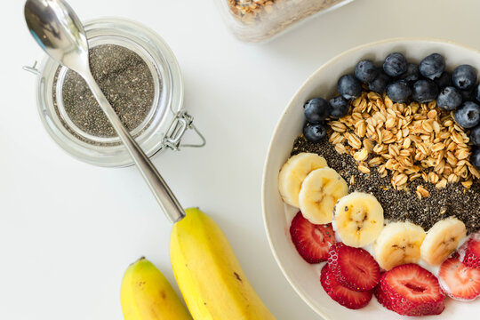White ceramic bowl is showing yogurt with banana, strawberry, blueberry rows on table, copy space