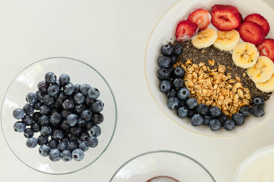 Ceramic bowl is being topped with granola, chia, fruit on table, bowl of blueberries, copy space