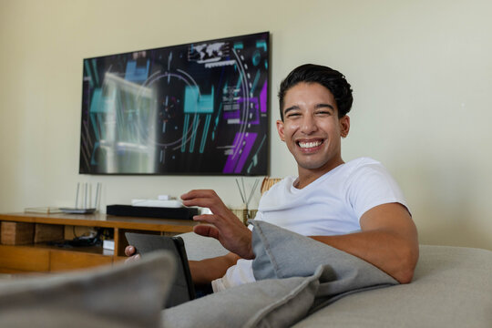 African American man reclining on sofa at home, holding tablet and watching wall TV, copy space