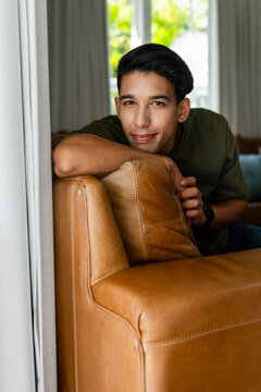 African American man leaning over tan leather sofa in living room, wearing olive shirt and watch