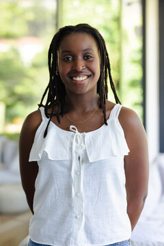 African American woman standing smiling near large windows wearing white ruffled blouse and denim