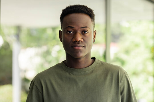 African adult male posing wearing olive crewneck tee with hoop earring on porch with posts
