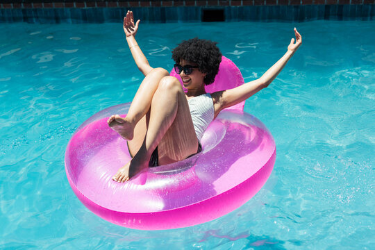 Bright pink inflatable ring with backrest is floating in clear blue pool, sunlight glinting