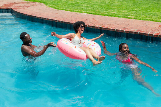 Pink donut float with sunglasses bobbing in clear pool water near brick coping and green lawn