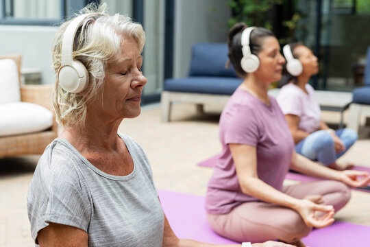 Diverse female classmates meditating on sunroom patio with yoga mats and headphones, copy space