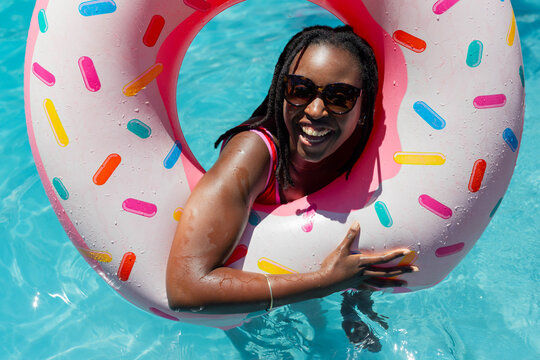 African American woman floating in pink donut, wearing sunglasses, bracelet glinting in pool