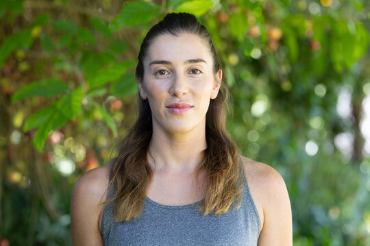 Adult female standing in garden wearing grey athletic tank top and pendant necklace, facing camera