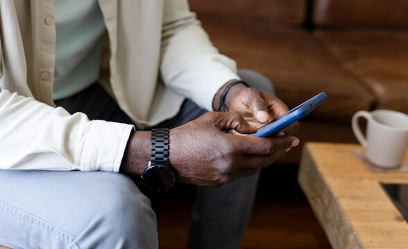 Blue smartphone being tapped by hands on leather sofa beside coffee table with mug and tablet