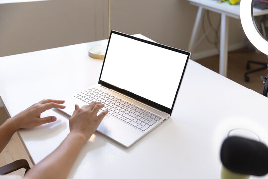 Silver laptop with blank white screen sitting on white desk near window, hands typing