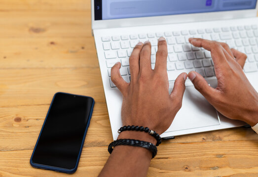 Hands are typing on white laptop keyboard on light wood table with blue phone nearby