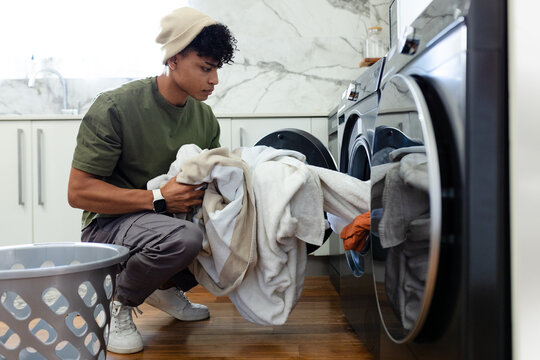Adult African American man crouching pulling towels, blanket from front-load washer in laundry room