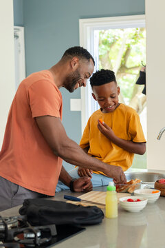 African American dad and son preparing snack at kitchen counter with wooden cutting board, backpack
