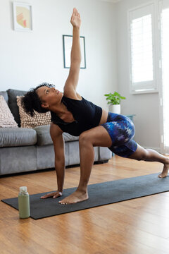 African American woman practicing yoga on black mat at home wearing black top and blue shorts