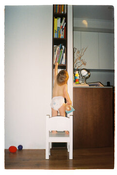 Toddler reaching for a book on a bookshelf at home - film analog
