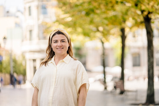 Smiling woman standing on city street with trees