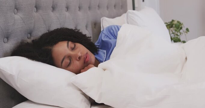 African American woman in blue satin pajamas lying in bed soft breath stirring pulling duvet waking