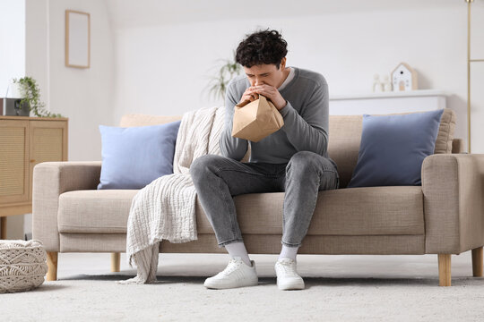 Young man with paper bag having panic attack on sofa at home