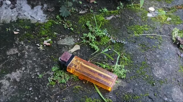 Footage of classic yellow plastic lighters placed on a hard textured surface overgrown with weeds