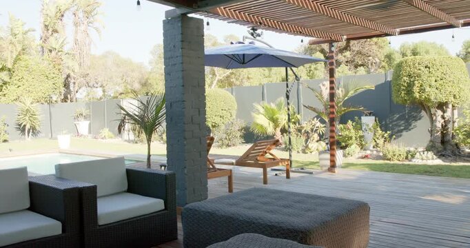 Camera is panning right and moving forward revealing patio seating ottoman pool umbrella backyard