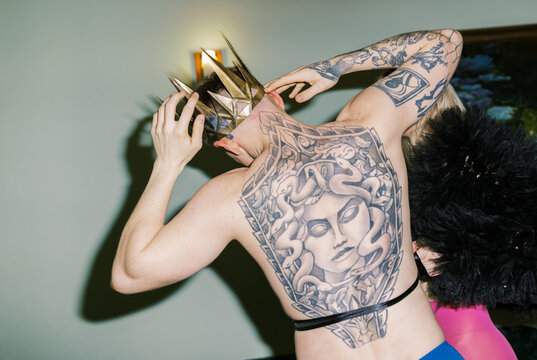 Person Wears Crown and Shows Large Back Tattoo in Event Setting