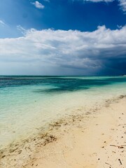 Obraz premium A picture perfect tropical Caribbean beach landscape. A sunny day. storm clouds out at sea. Turquoise and teal water is crystal clear. Fine white powder sand stretches across the tide andcoastline. 