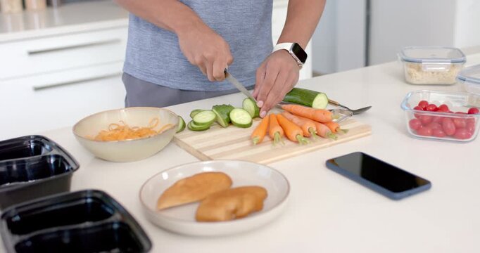 Adult picking up chef's knife at kitchen counter, slicing zucchini into rounds for meal prep