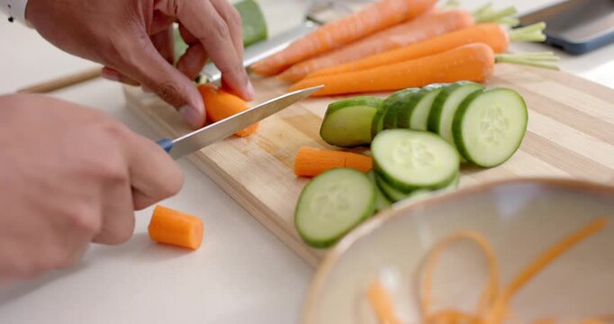 First-cut starting, hands are slicing carrots into rounds on board at kitchen counter for salad