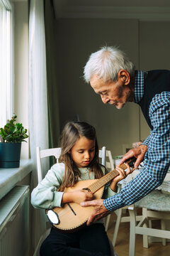 Senior man teaching how to play a mandolin to his granddaughter