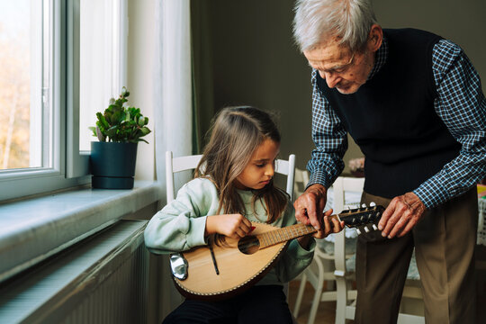 Senior man teaching how to play a mandolin to his granddaughter