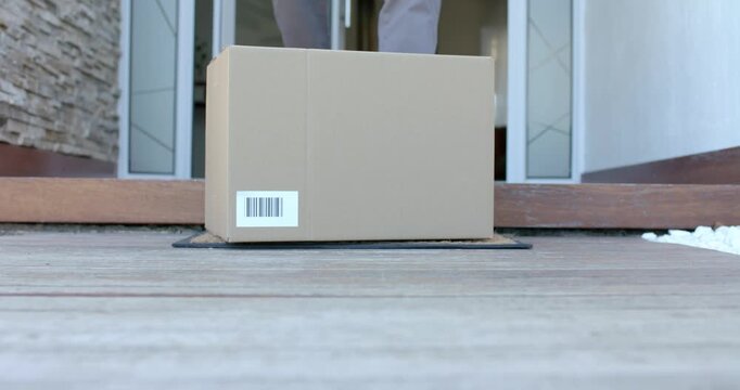 African American man retrieving package from coir doormat, reaching and lifting box over threshold
