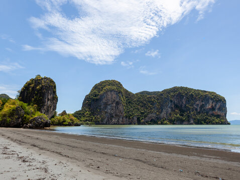 Hat Ratcha Mongkhon beach in Sikao District, Trang, Thailand. Tropical coastline with scenic rock formations. Clear blue sea and sandy shore under cloudy sky.
