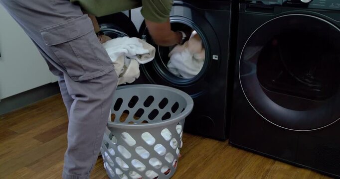 Man is opening left washer, pulling white towels from basket into washer for washing at home