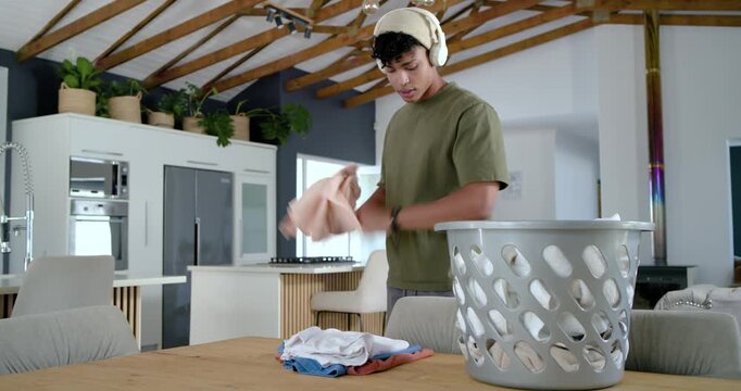 African American man with headset reaching into laundry bin, folding items on table organizing