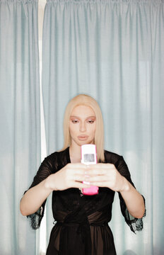 Person Poses With Phone in Front of Blue Curtains