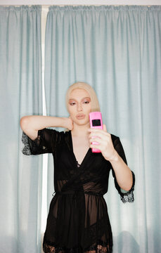 Person Poses With Phone in Front of Blue Curtains
