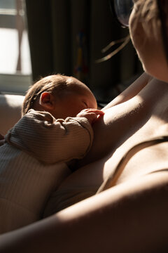 Mother breastfeeding newborn baby in window light