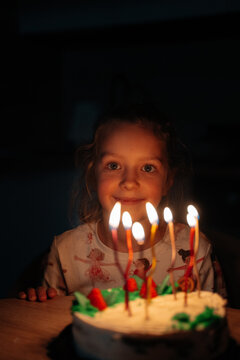Girl smiling in front of birthday cake with lit candles 7 years old