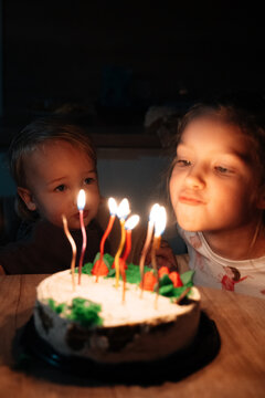 Children blowing birthday candles together at night