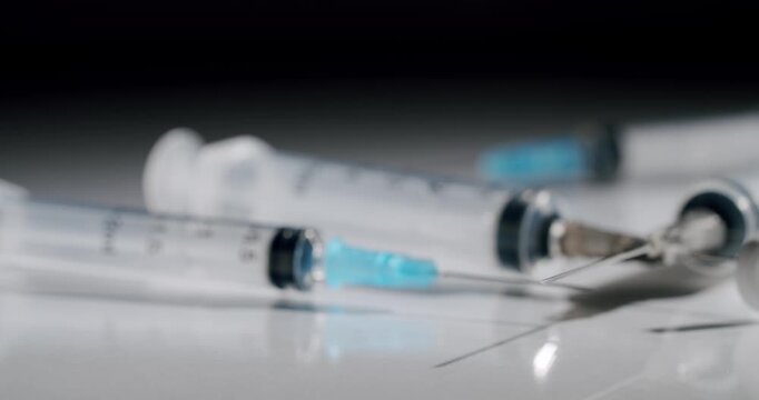 Empty plastic medical syringes with sharp needles lying on a reflective white surface against a dark background, representing healthcare, vaccination, or medical procedures